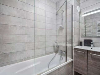 This modern bathroom features a sleek bathtub with a glass shower screen, perfect for a relaxing soak or a quick shower.