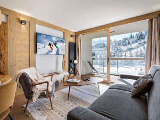 Experience luxurious mountain living in this beautifully appointed living room, featuring a large flat-screen TV displaying a vibrant ski scene and a cozy armchair draped with a plush throw.