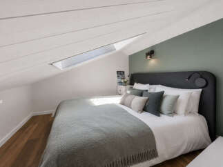 Discover this charming attic bedroom, featuring a cozy bed with plush pillows and a soft grey throw.