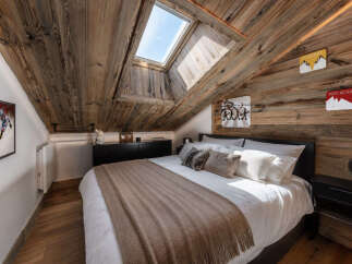 Experience rustic charm in this attic bedroom, featuring a cozy bed adorned with plush pillows and a warm throw blanket.