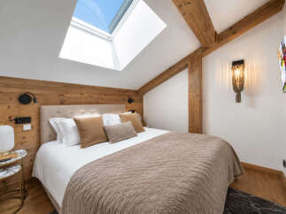 Experience ultimate comfort in this charming attic bedroom, featuring a luxurious bed adorned with plush pillows and a cozy duvet.
