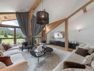 Experience luxurious mountain living in this stunning chalet, featuring a spacious living area with vaulted ceilings and exposed wooden beams.
