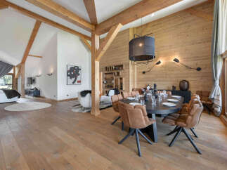 Experience luxury mountain living in this stunning open-plan dining and living area, featuring exposed wooden beams and a warm, natural wood-paneled wall.