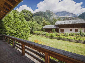 Experience the charm of mountain living with this stunning property, featuring a rustic wooden deck overlooking a lush green lawn and a picturesque alpine backdrop.
