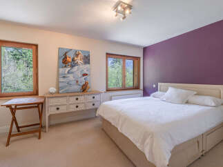 This charming bedroom features a comfortable bed with crisp white linens, accented by a striking purple accent wall.