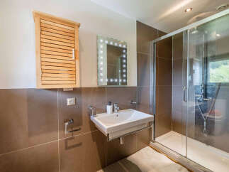 This modern bathroom features a sleek white sink mounted on a chrome stand, complemented by a wooden slatted medicine cabinet and a lighted mirror.