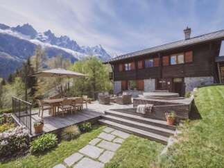 Experience luxury mountain living in this stunning chalet, featuring a spacious wooden deck with a dining area and comfortable lounge seating.