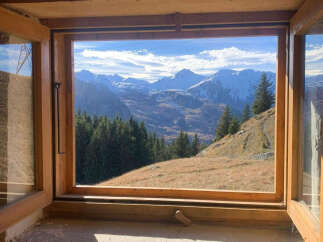 Experience breathtaking mountain views from this charming property, framed by a rustic wooden window.