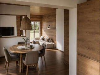 Experience modern living in this beautifully designed open-concept space, featuring a cozy dining area with a round wooden table and comfortable chairs, seamlessly flowing into a spacious living room with a plush sectional sofa and warm wood-paneled walls.