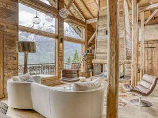 Experience breathtaking mountain views from this stunning log cabin living room, featuring a plush white curved sofa and a cozy brown leather armchair.