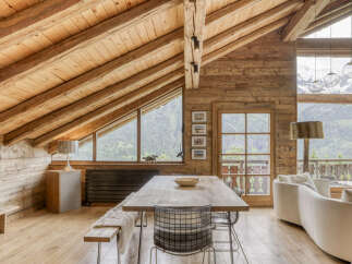 Experience rustic luxury in this stunning mountain chalet, featuring a vaulted wood-beamed ceiling and panoramic windows showcasing breathtaking alpine views.
