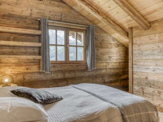 Experience rustic charm in this cozy attic bedroom, featuring exposed wooden beams and walls that exude warmth and character.