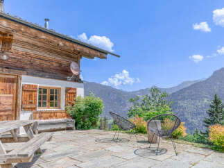 Experience breathtaking mountain views from this charming wooden chalet, featuring a spacious stone patio perfect for outdoor dining and relaxation.
