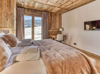 Experience cozy mountain living in this charming bedroom, featuring a plush bed adorned with soft throws and a stunning view of a snowy landscape through French doors.