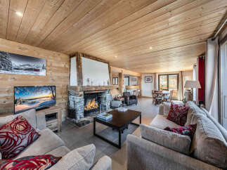 Experience cozy mountain living in this charming living room, featuring a rustic stone fireplace and warm wood-paneled walls.