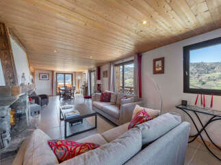 Experience cozy mountain living in this charming living room, featuring a grand stone fireplace and a warm, wood-paneled ceiling.