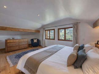 Experience cozy mountain living in this charming bedroom featuring exposed wooden beams and a picturesque view from the windows.
