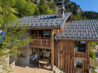 Experience the charm of this mountain chalet, featuring a rustic stone and wood exterior nestled amidst lush greenery.