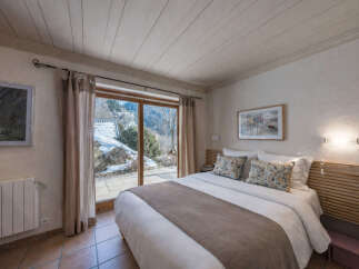 Experience cozy mountain living in this charming bedroom featuring a comfortable bed and stunning views of a snowy landscape through a large sliding glass door.