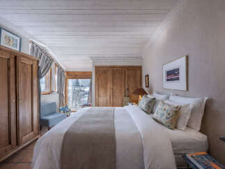Experience rustic charm and cozy comfort in this inviting bedroom, featuring a large wooden wardrobe and a plush bed adorned with decorative pillows.