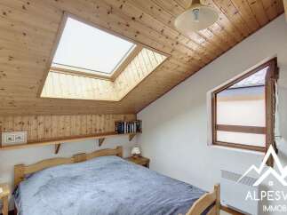 Discover this charming attic bedroom featuring a unique sloped wooden ceiling and a large skylight that floods the space with natural light.