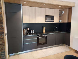 Discover this modern kitchen featuring sleek dark cabinetry contrasted with light wood upper cabinets and a stylish black backsplash.