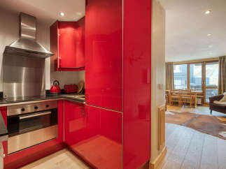 Experience modern living in this stylish apartment featuring a sleek red kitchen with stainless steel appliances and ample cabinet space.