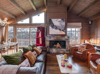 Experience rustic luxury in this stunning mountain chalet living room, featuring a grand stone fireplace and exposed wooden beams.