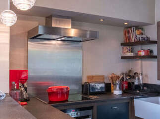 This modern kitchen features a sleek stainless steel range hood and backsplash, complemented by a vibrant red pot on the induction stovetop.