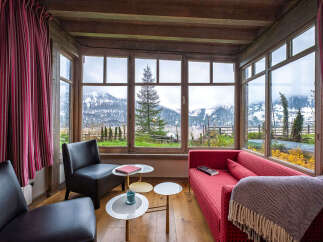 Experience breathtaking mountain views from this cozy living area, featuring a vibrant red sofa and comfortable seating.