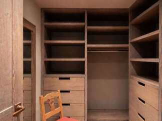 Step into this spacious walk-in closet, featuring custom-built wooden shelving and drawers for ample storage.