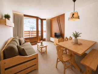 Experience cozy mountain living in this charming apartment, featuring a comfortable sofa and a rustic wooden dining set perfect for family meals.
