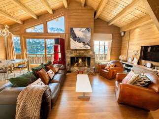 Experience luxury mountain living in this stunning chalet featuring a grand stone fireplace and expansive windows with breathtaking alpine views.