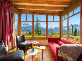 Experience breathtaking mountain views from this cozy living space, featuring a vibrant red sofa and comfortable armchairs perfect for relaxation.