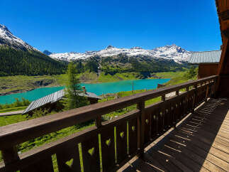 Experience breathtaking mountain views from this charming wooden balcony, overlooking a stunning turquoise lake and snow-capped peaks.