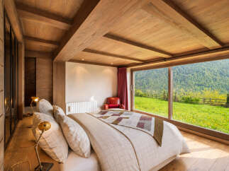 Experience breathtaking mountain views from this stunning bedroom, featuring a cozy bed and a large window overlooking a lush green landscape.