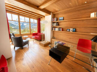 Experience breathtaking mountain views from this stunning living room, featuring a cozy red sofa and a comfortable grey armchair perfect for relaxation.