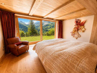 Experience breathtaking mountain views from this luxurious bedroom, featuring a cozy leather armchair and a plush, quilted bed.