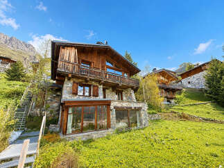 Experience luxury mountain living in this stunning chalet, featuring a rustic stone and wood facade nestled amidst breathtaking alpine scenery.