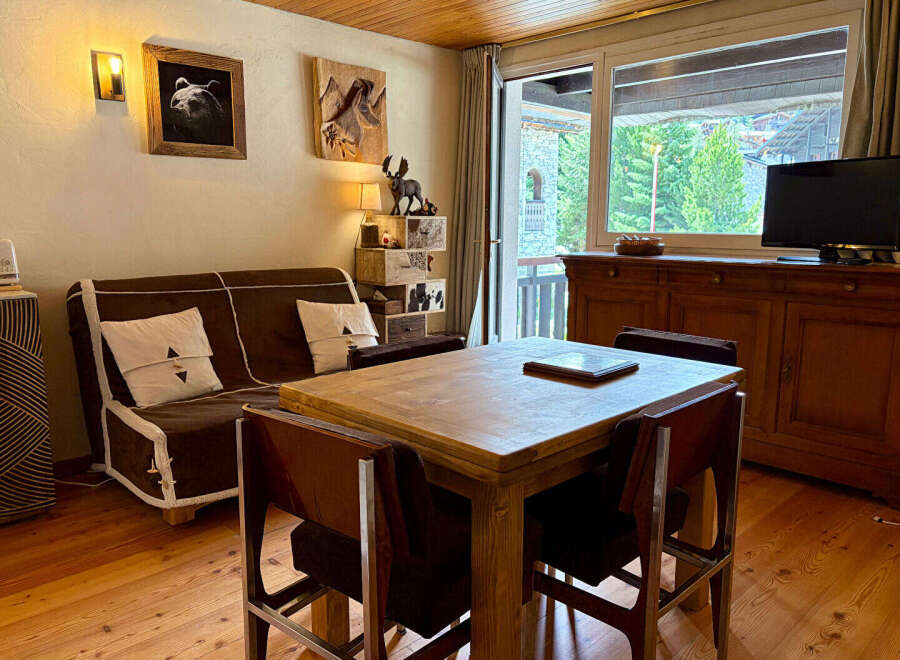 Experience cozy mountain living in this charming apartment, featuring a comfortable sofa and a rustic wooden dining table perfect for family meals.