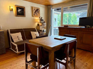 Experience cozy mountain living in this charming apartment, featuring a comfortable sofa and a rustic wooden dining table perfect for family meals.