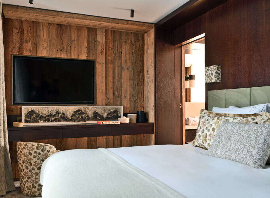 Experience rustic luxury in this beautifully appointed bedroom, featuring a large flat-screen TV mounted on a warm, wood-paneled wall.