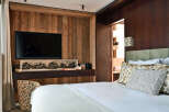 Experience rustic luxury in this beautifully appointed bedroom, featuring a large flat-screen TV mounted on a warm, wood-paneled wall.