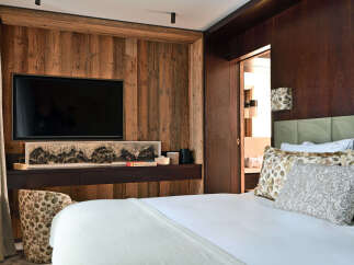 Experience rustic luxury in this beautifully appointed bedroom, featuring a large flat-screen TV mounted on a warm, wood-paneled wall.