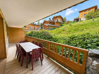 Enjoy outdoor dining on this charming wooden deck, complete with a table and chairs, offering stunning views of the surrounding green hillside and traditional alpine architecture.