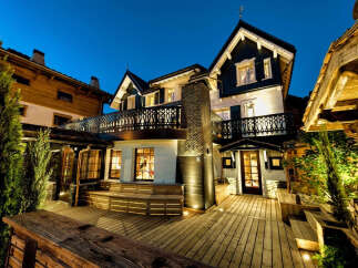 Experience luxury mountain living in this stunning chalet, featuring a spacious wooden deck perfect for après-ski gatherings.