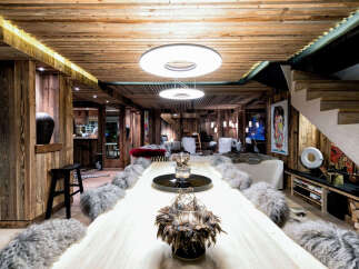Experience rustic luxury in this stunning chalet-style living space, featuring warm wood paneling throughout and a grand dining table perfect for gatherings.