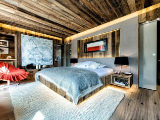 Experience luxurious mountain living in this stunning chalet bedroom, featuring rustic wood-paneled walls and ceiling, complemented by modern recessed lighting.