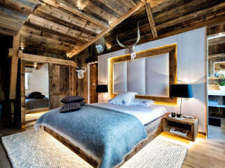 Experience rustic luxury in this stunning mountain chalet bedroom, featuring a king-size bed with a plush blue throw and a striking upholstered headboard.