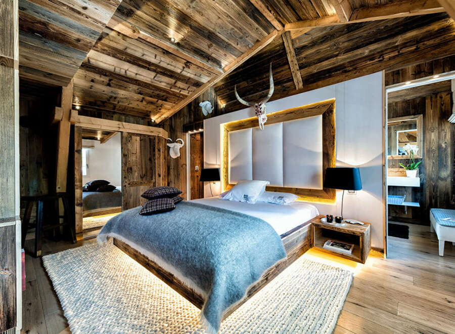 Experience rustic luxury in this stunning chalet bedroom, featuring a king-sized bed with a plush blue throw and a striking upholstered headboard.